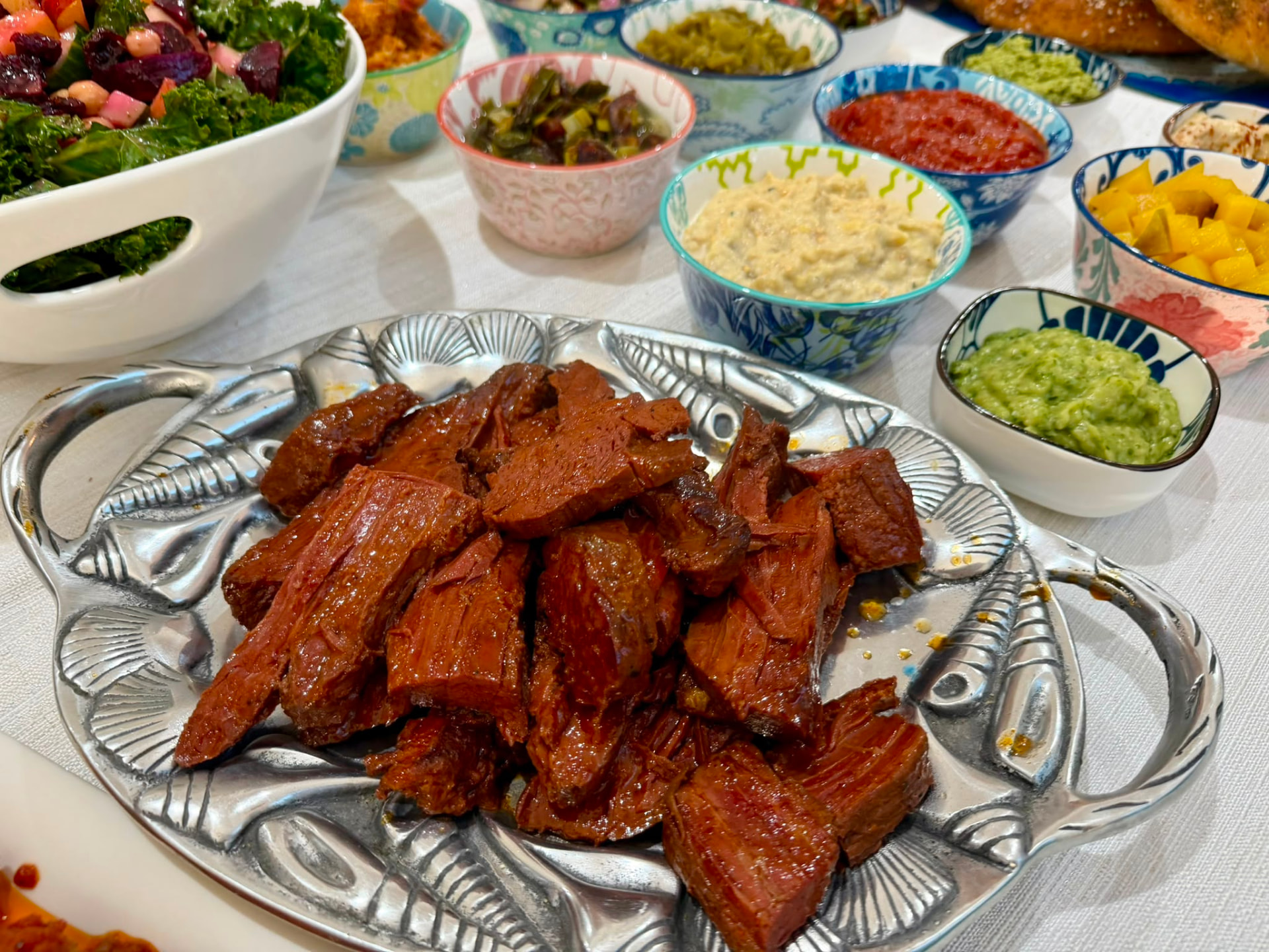Sliced corned beef on a silver platter surrounded by bowls of Israeli dips